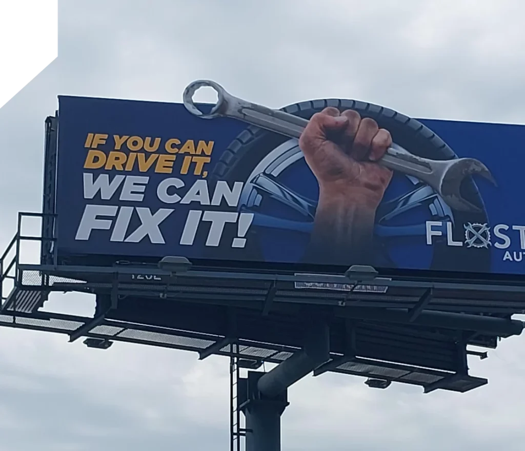 FloState Auto Diesel Repair in St. Cloud, FL. A billboard displaying an image of a person's hand holding a large wrench, with a tire in the background. The text reads, "IF YOU CAN DRIVE IT, WE CAN FIX IT!" The logo for "FLOSTERS AUTO" is visible on the right side. The sky is cloudy.