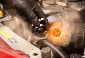 Close-up of a mechanic’s gloved hand removing a radiator cap with steam rising, highlighting the importance of maintaining proper coolant levels and regular inspections to prevent diesel engine overheating.