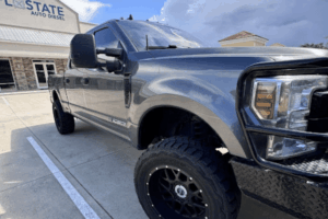 Discover the Absolute Best Diesel Repair in St. Cloud, FL: Why FloState Auto Diesel Repair Stands Out. A large, lifted gray pickup truck is parked in front of a building with a sign that reads State Auto Diesel. The truck has black off-road tires and a shiny exterior, set against a partly cloudy sky.
