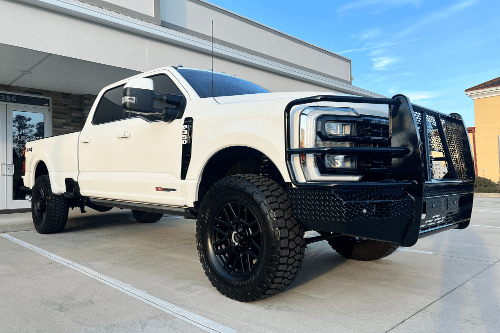 diesel engine maintenance, diesel repair in St. Cloud, FL at FloState Auto Diesel Repair. A white heavy-duty pickup truck equipped with off-road tires and a custom black grille guard, parked in front of an auto repair shop.