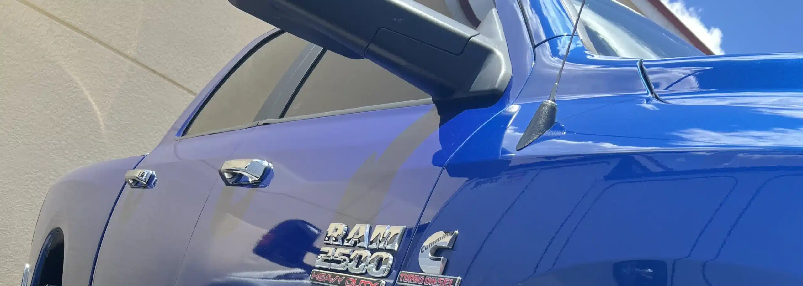 Close-up of the side mirror and badge of a blue RAM 2500 truck with a Cummins badge, highlighting its robust engineering. The truck emphasizing the quality you can expect from Dodge Cummins diesel repair shops.