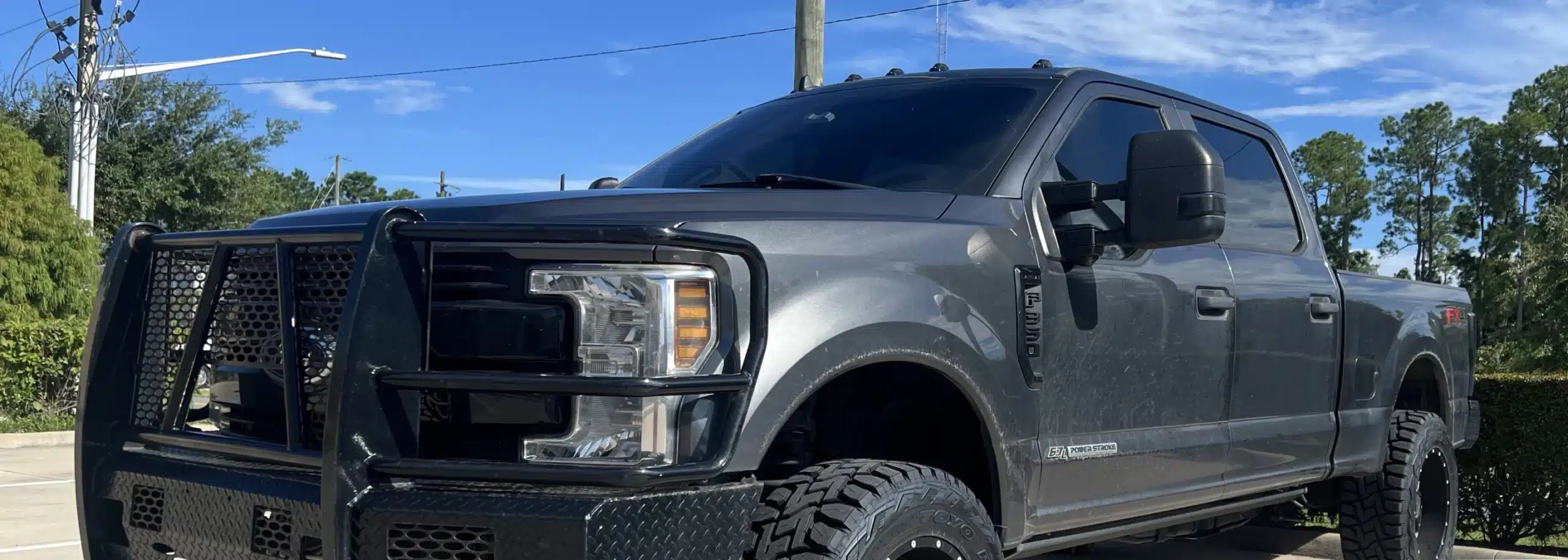 A dark-colored Ford pickup truck parked on a road with trees in the background showcases its rugged elegance. The imag, hints at the powerful capabilities of a Power Stroke engine.