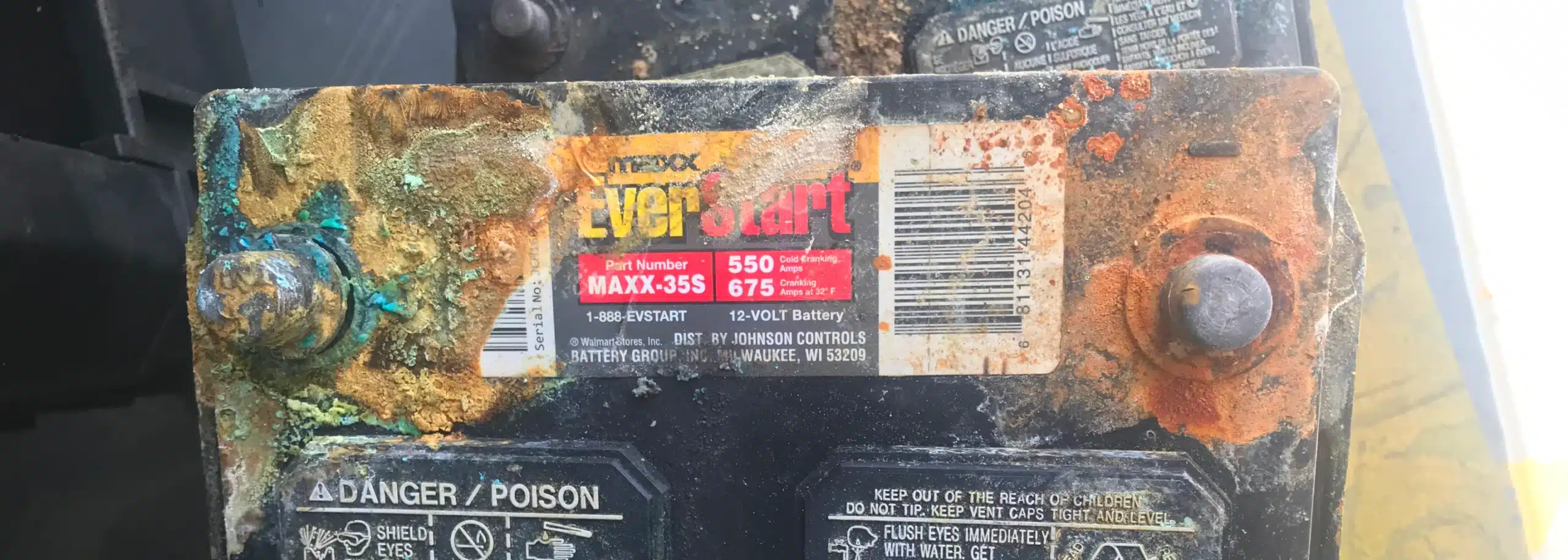 A close-up of a weathered car battery with corroded terminals highlights the importance of preventative maintenance. The EverStart label details specifications: 550 CCA, 435 A, and 675 CA. Hazard warnings are clear, indicating poison and corrosive materials present.