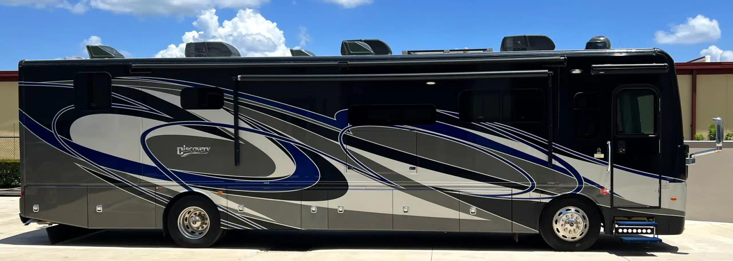 A large motorhome showcasing a sleek design and swirling patterns on the side, sits parked outdoors on a clear day. Its roof holds several air conditioning units, testament to recent RV maintenance services that ensure journeys remain cool and comfortable.