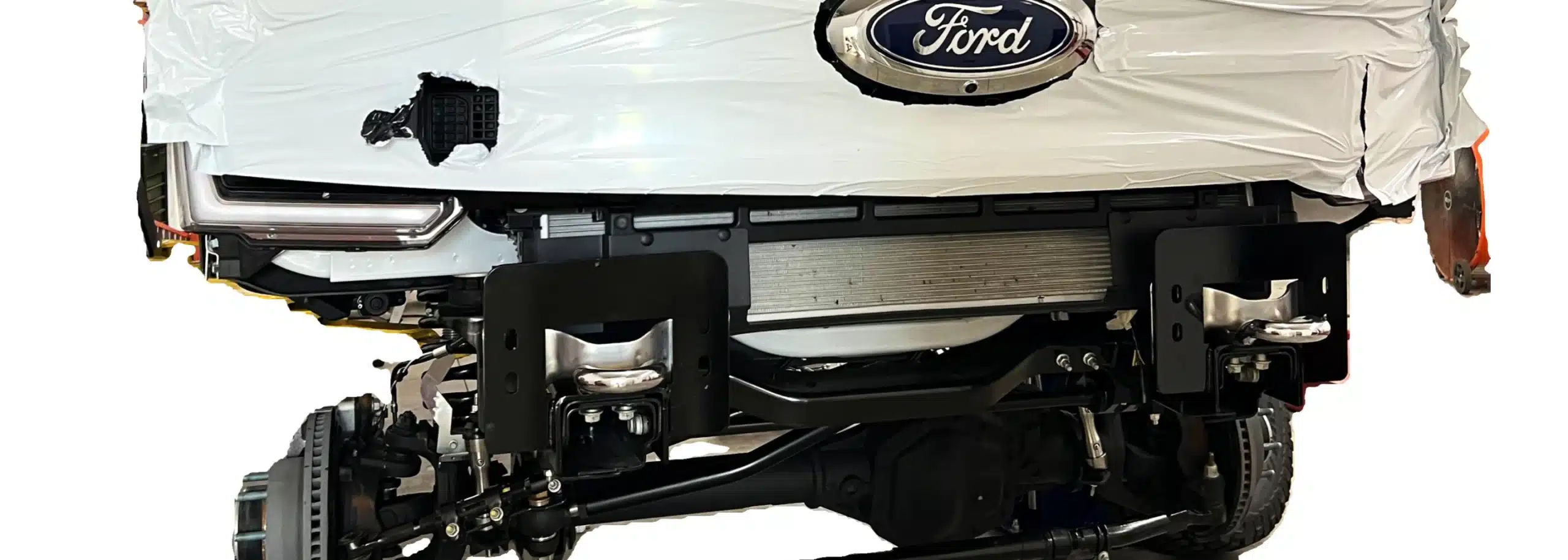 Close-up of a Ford vehicle's front, partially covered, showcasing mechanical components like the suspension and radiator. The Ford emblem stands proudly at the top.