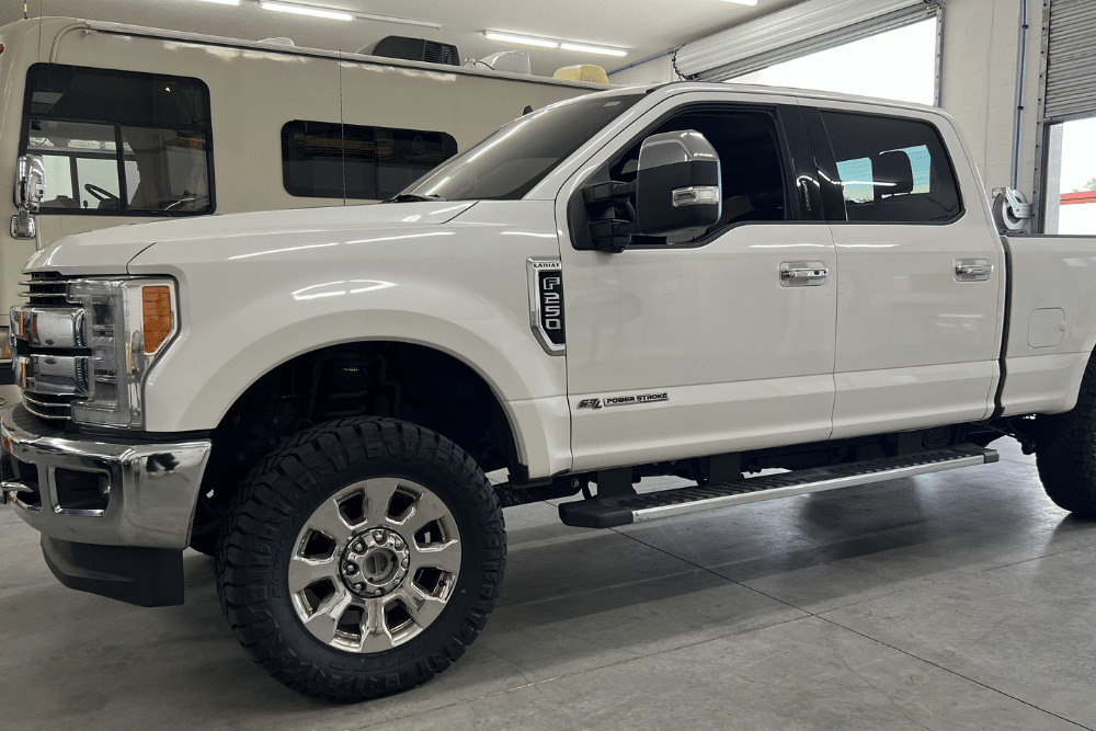 light-duty truck maintenance, diesel repair in St. Cloud, FL at FloState Auto Diesel Repair. White Ford F-250 Power Stroke pickup truck with off-road tires parked inside a garage with an RV in the background.