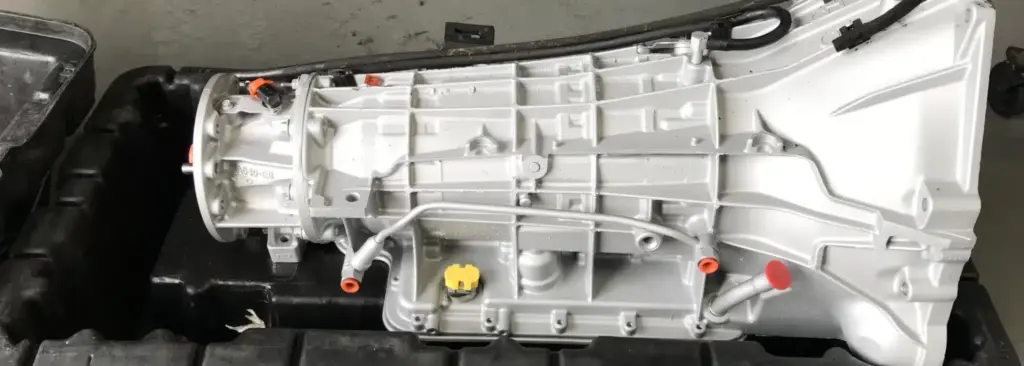 A close-up of a mechanical component with gears and cables, partially painted in white and reminiscent of a transmission service and there’s a black pattern on the bottom right corner.
